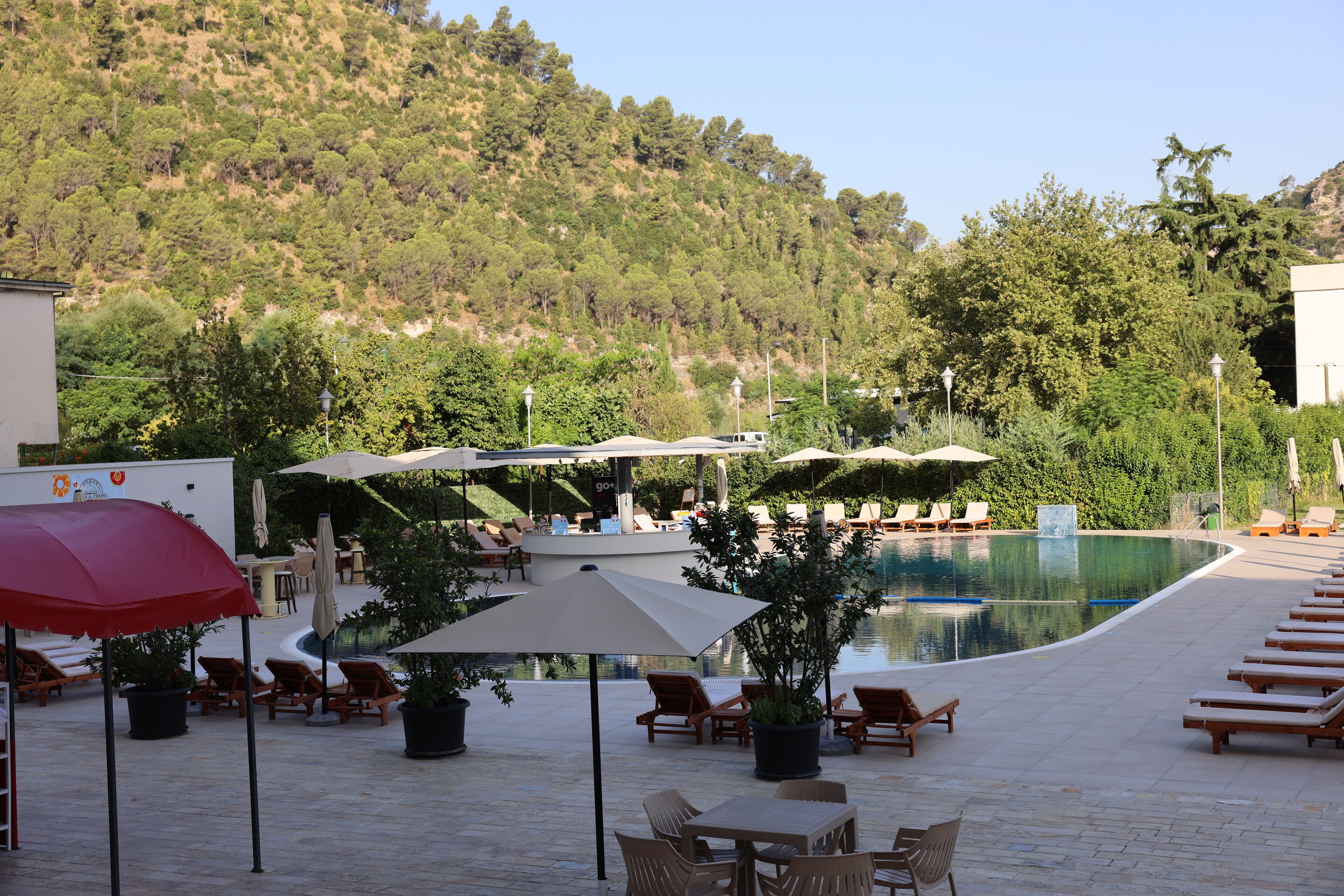 A poolside area with lounge chairs, umbrellas, and a view of a hillside.