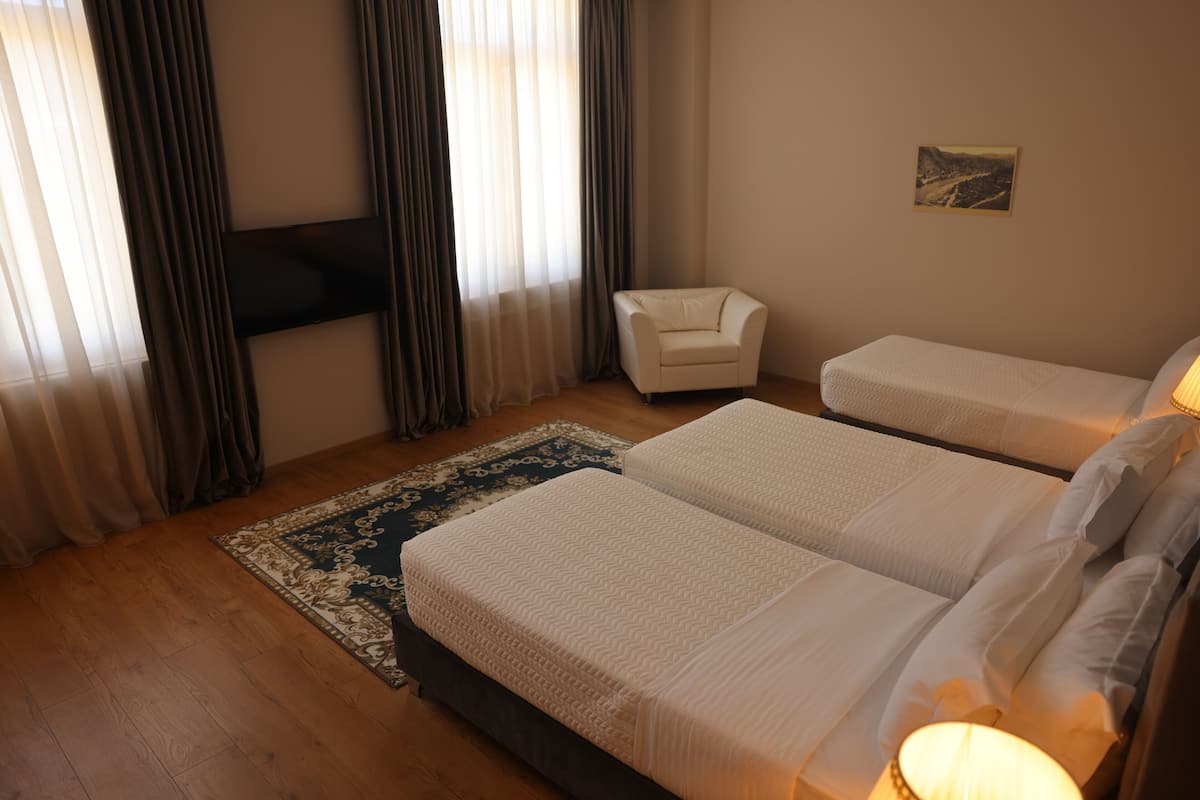Quarto de hotel com duas camas, uma poltrona, televisão na parede e tapete no chão.
