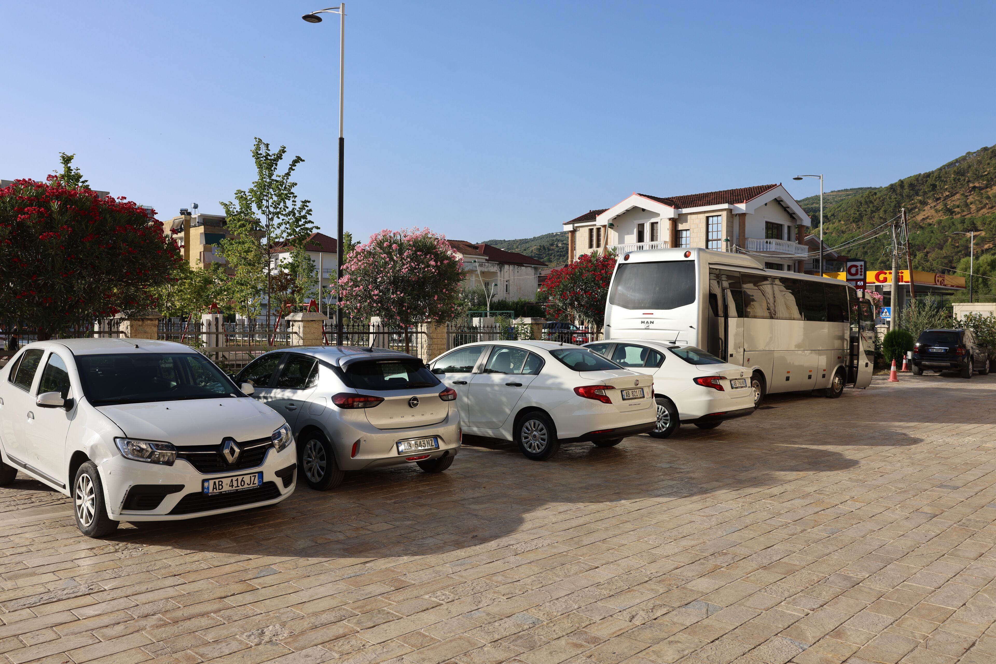 A parking lot with several cars and a bus, surrounded by buildings and trees.