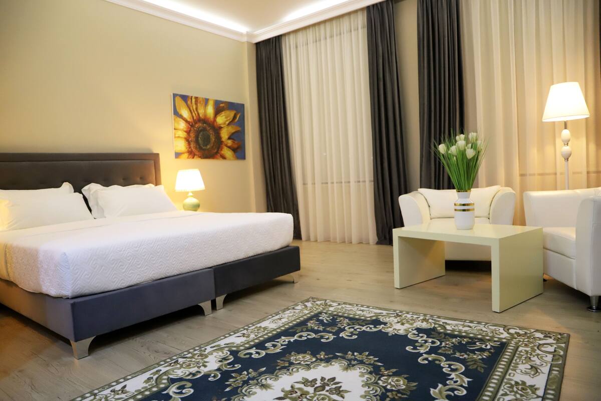 Quarto de hotel com cama, escrivaninha, cadeira, abajur e um quadro de um girassol.