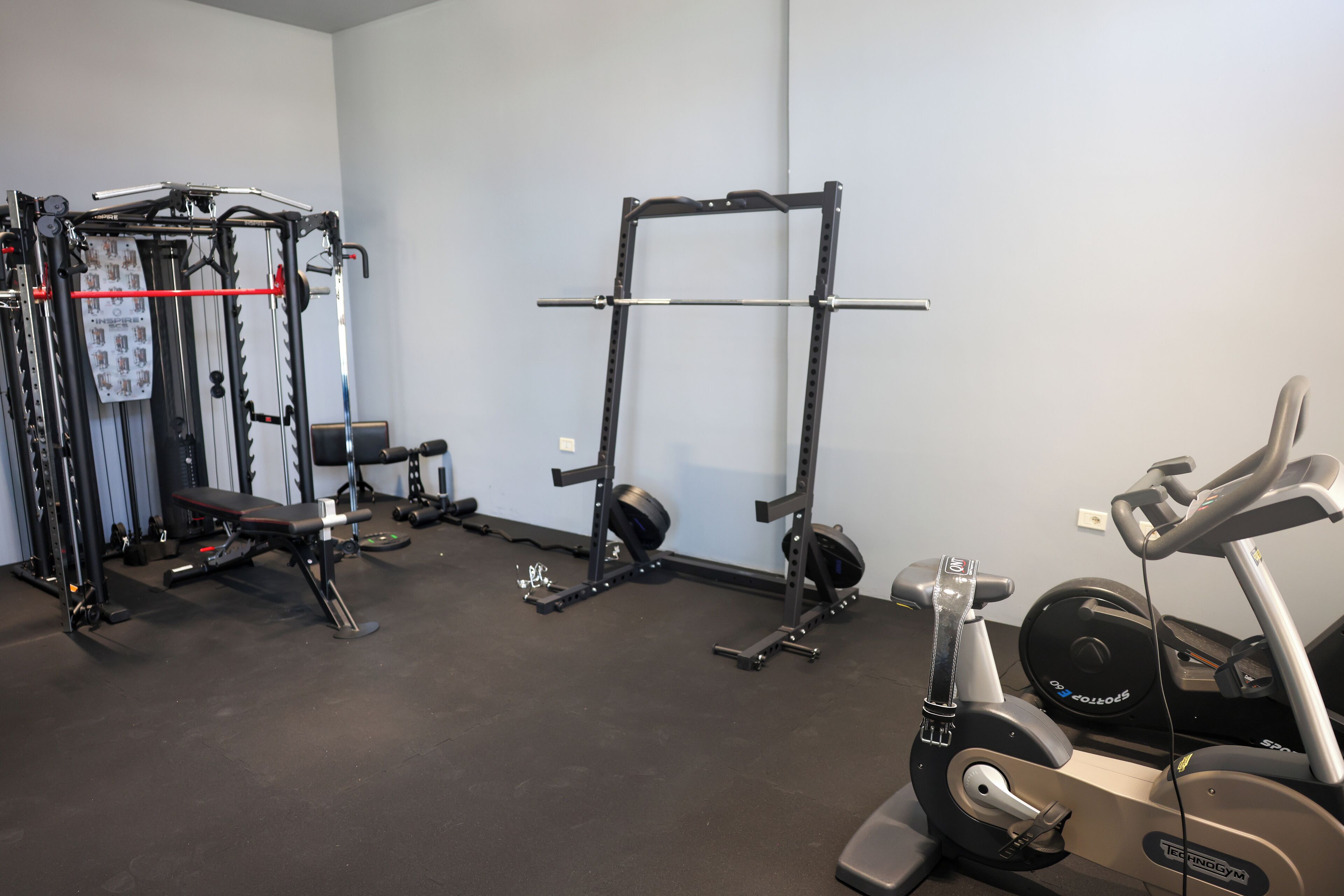 A gym with a bench press, squat rack, and an elliptical machine.