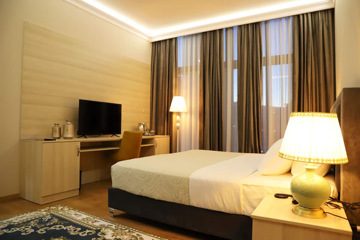 Quarto de hotel com cama, escrivaninha, televisão e duas luminárias.