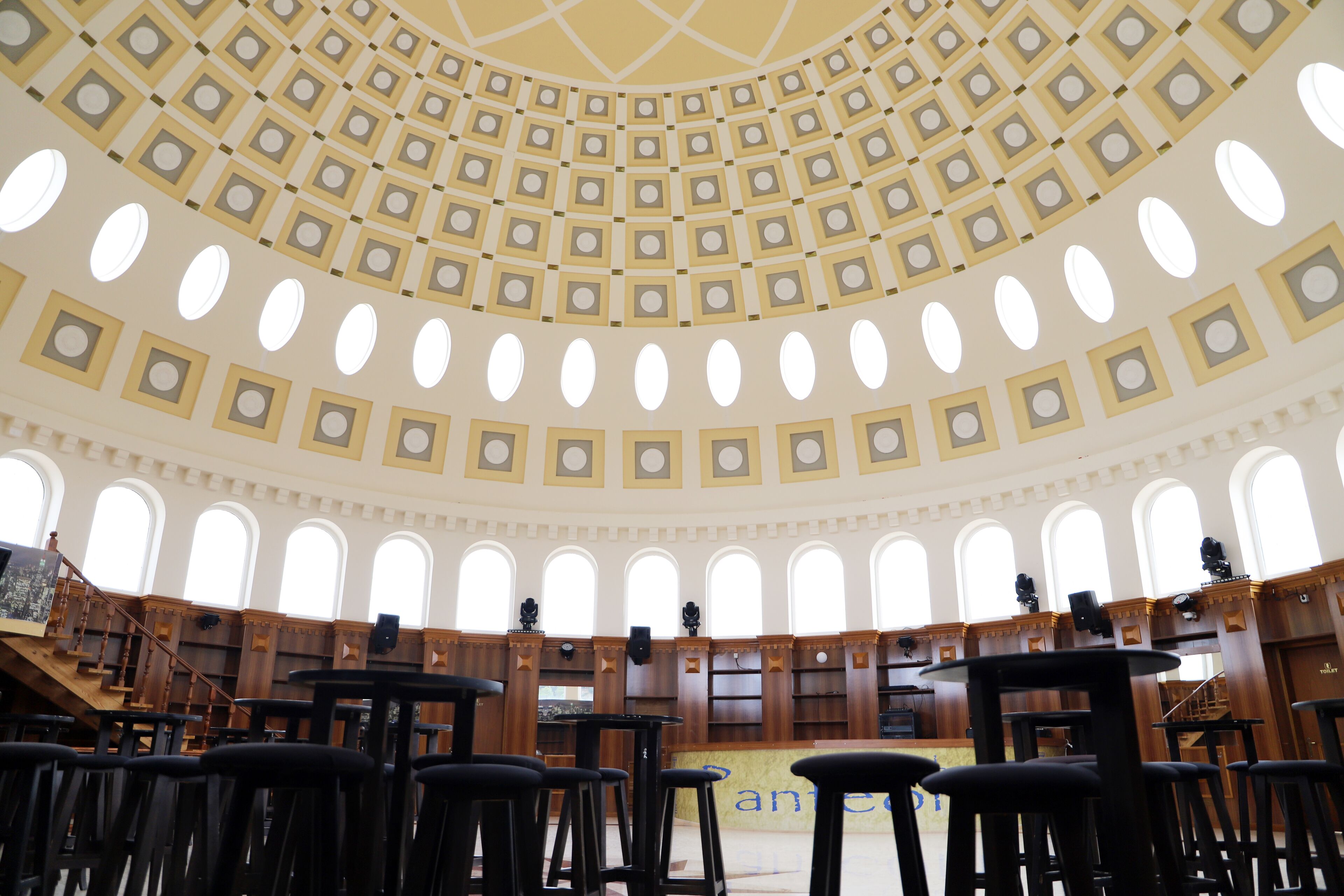 Een bibliotheekinterieur met een koepelplafond, meerdere leestafels en boekenplanken.