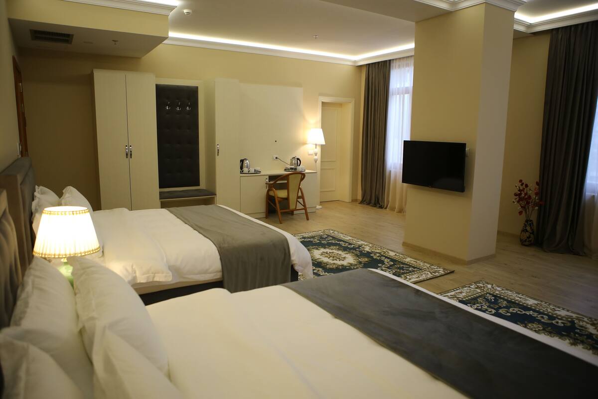 Quarto de hotel com duas camas, uma escrivaninha, televisão e banheiro.