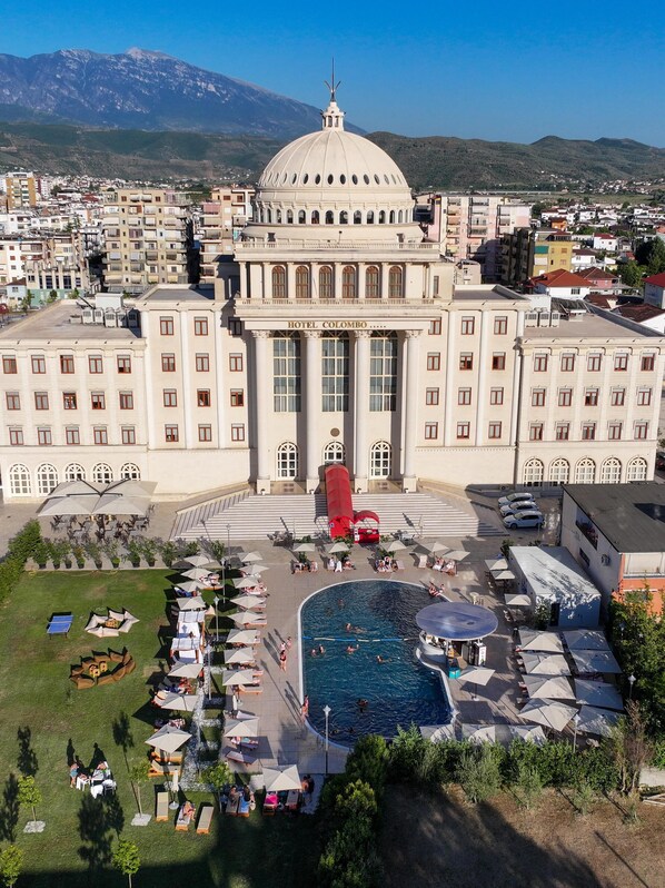 A large hotel with a prominent dome, a swimming pool, and outdoor seating areas. - Hotel Colombo (Berat)