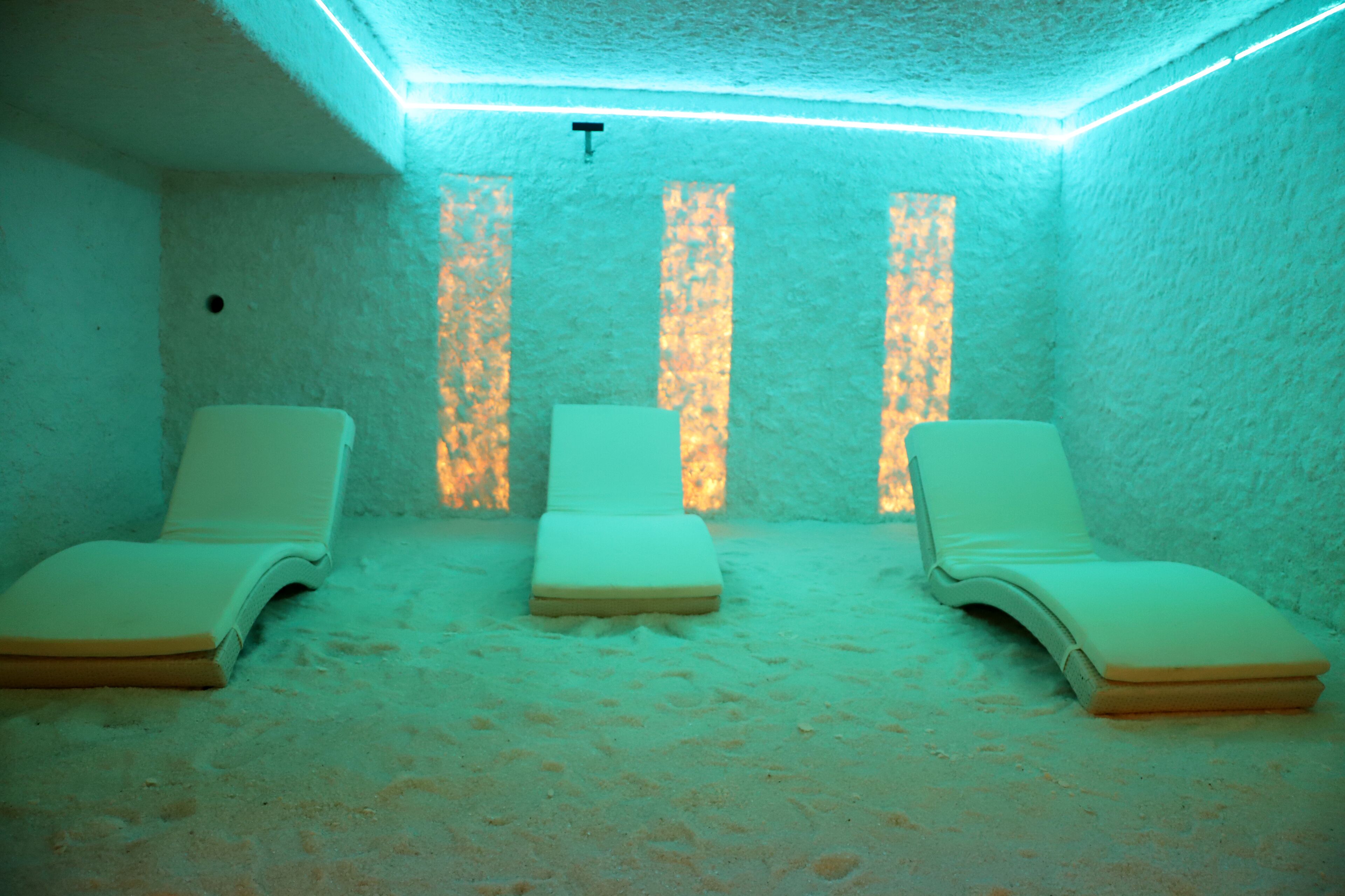 A room with three sunbeds, a textured wall, and a ceiling with linear lights.