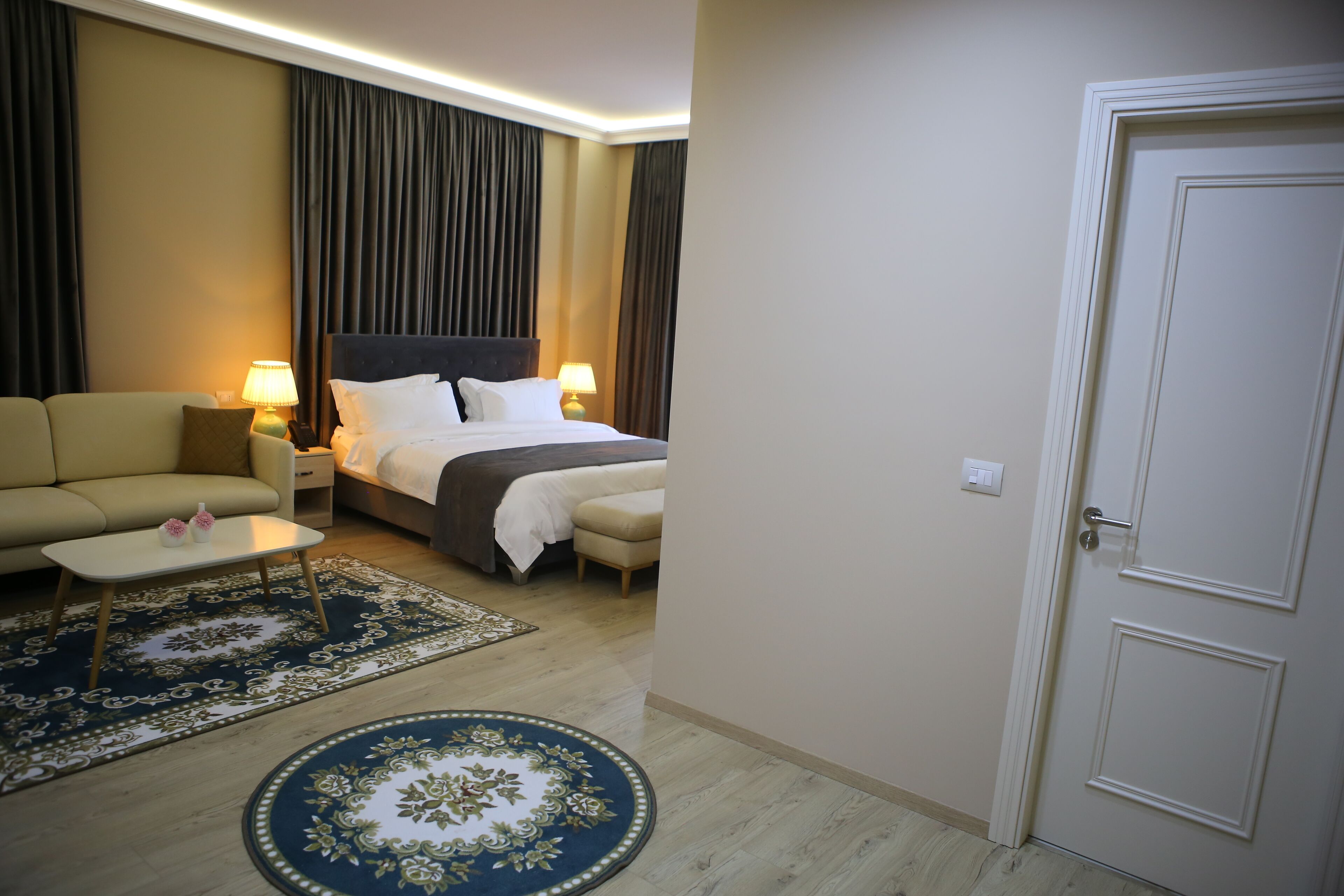 A hotel room with a bed, a sofa, a coffee table, and a door.