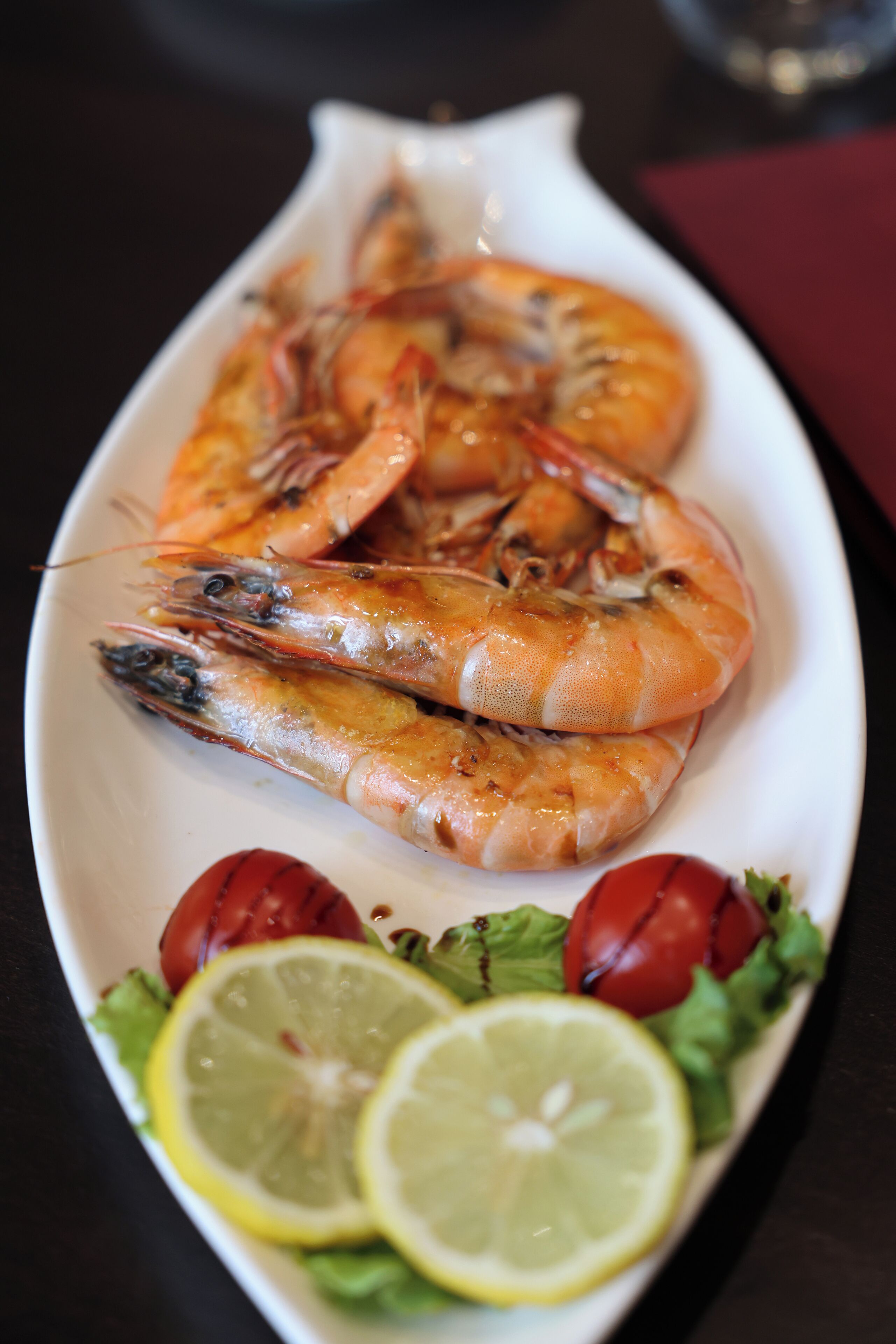 A plate of cooked shrimp with lemon slices and cherry tomatoes.