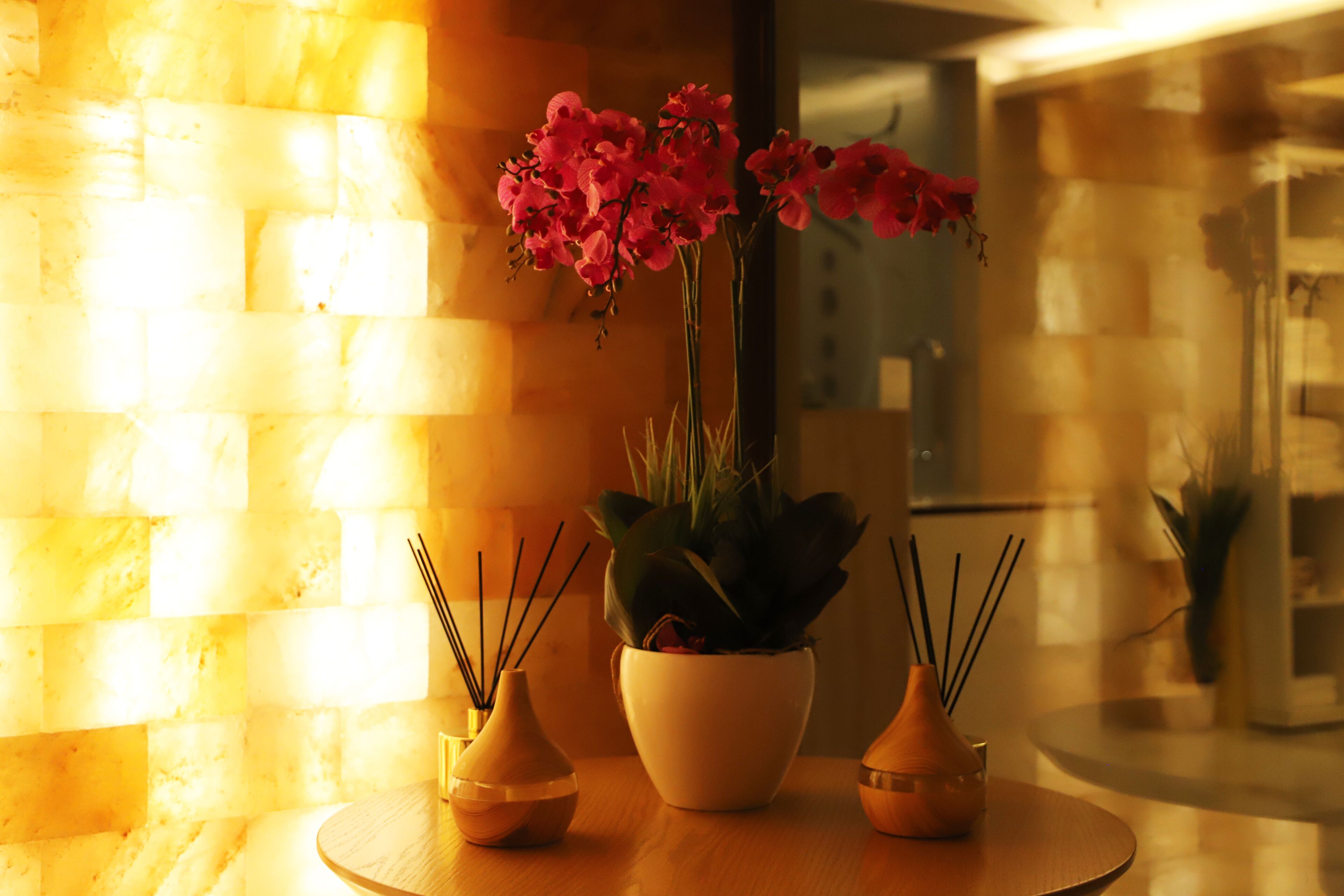 A table with three vases, one with pink flowers, and a brick wall in the background.