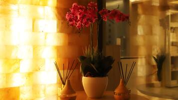 A table with three vases, one with pink flowers, and a brick wall in the background.