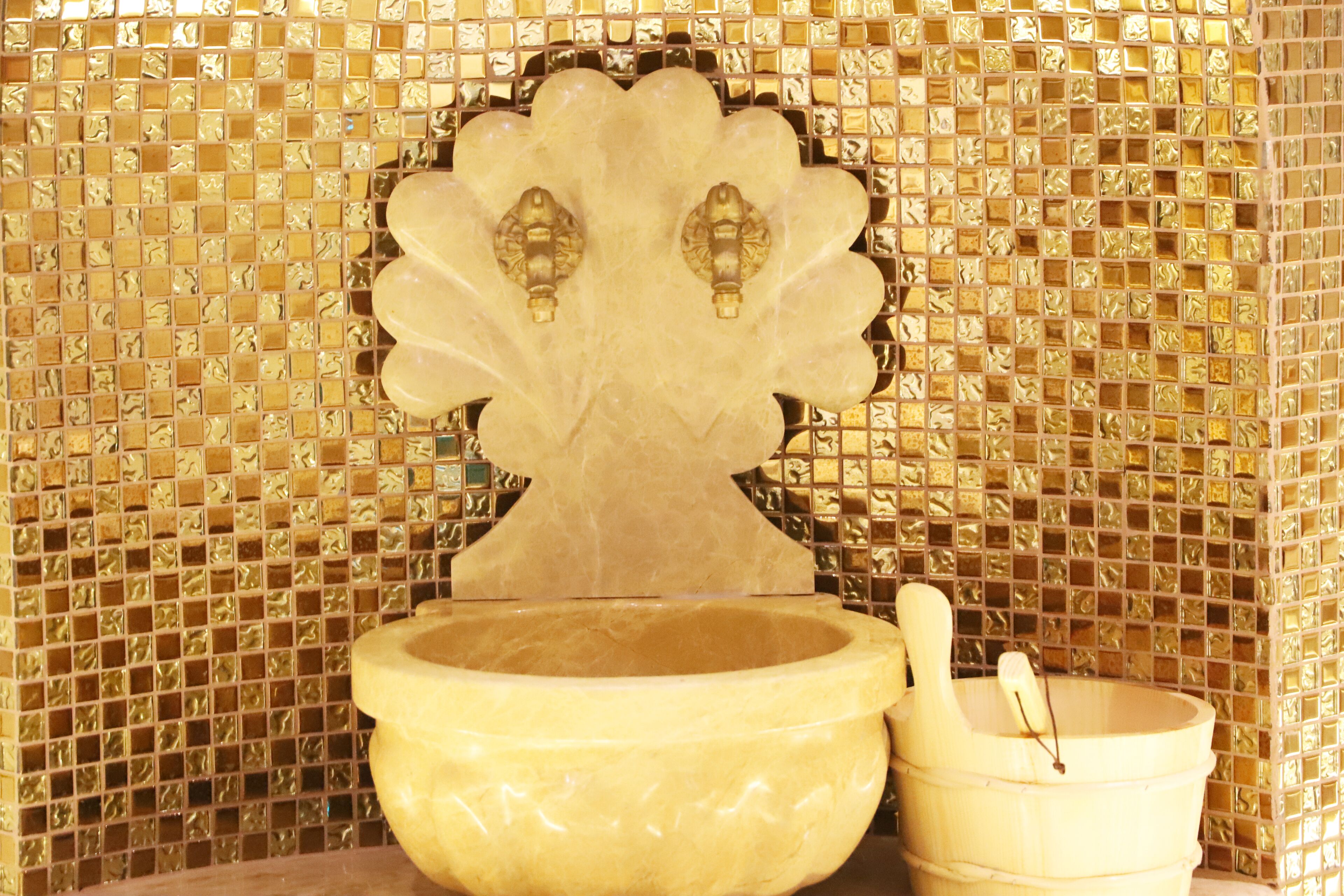 A bathroom with a mosaic tile wall, a large basin, and a wooden bucket.