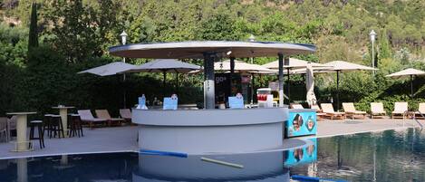 Un área de piscina con bar, sillones y sombrillas.