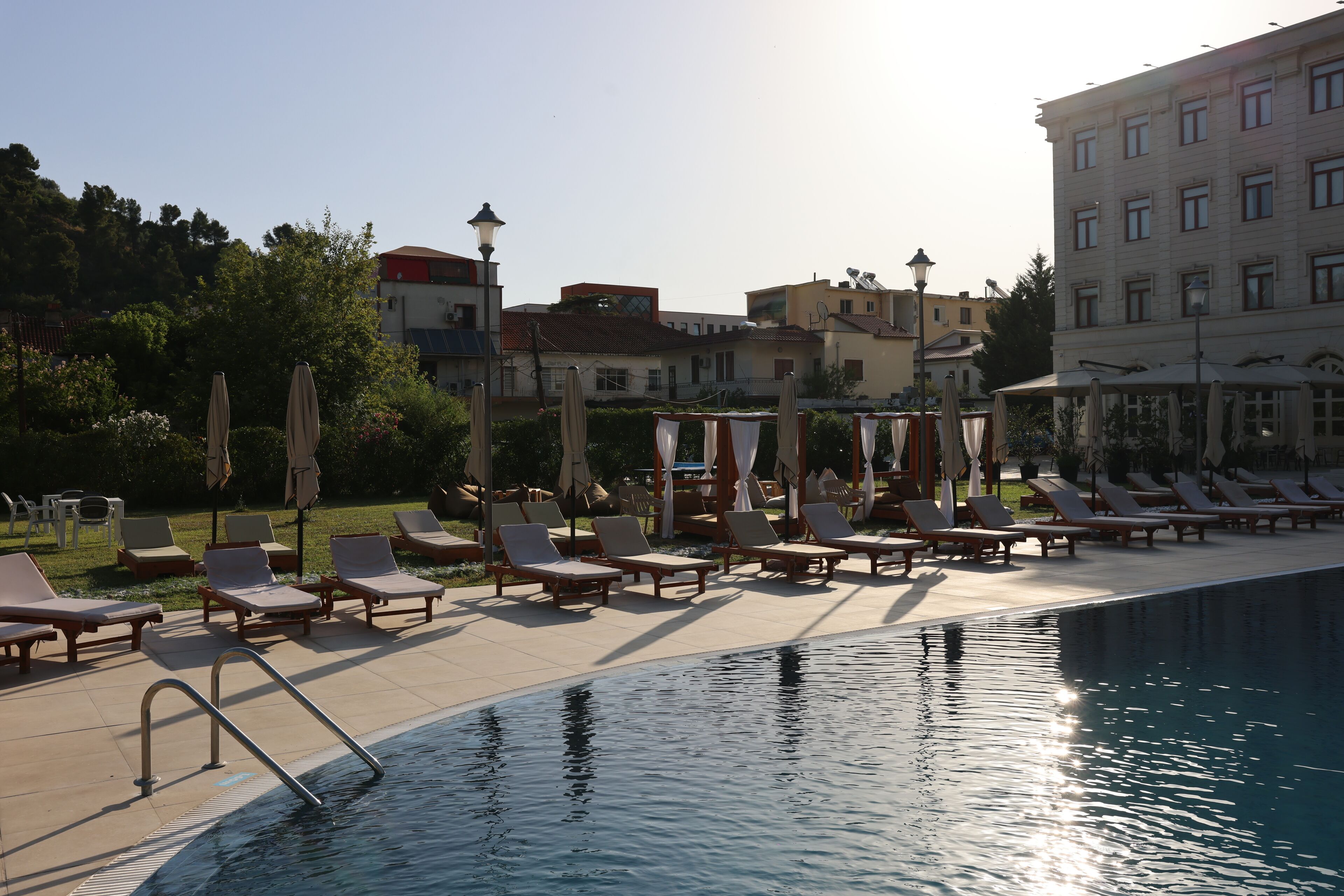 Un espace aménagé au bord de la piscine, avec des chaises longues et des parasols, une piscine, et des bâtiments en arrière-plan.