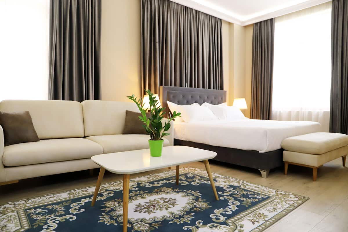 Quarto de hotel com cama, sofá, mesa de centro e um vaso de planta.