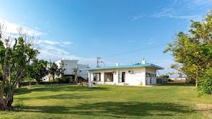 A two-story house with a blue roof, surrounded by a well-maintained lawn and trees. - Green Beach le Island (Ie)
