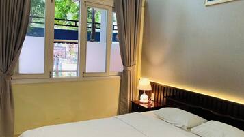 A hotel room with a bed, a nightstand with a lamp, a window with curtains, and a wall-mounted picture.