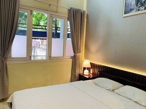 Hotelkamer met een bed, nachtkastje met lamp, raam met gordijnen en een aan de muur hangend schilderij.