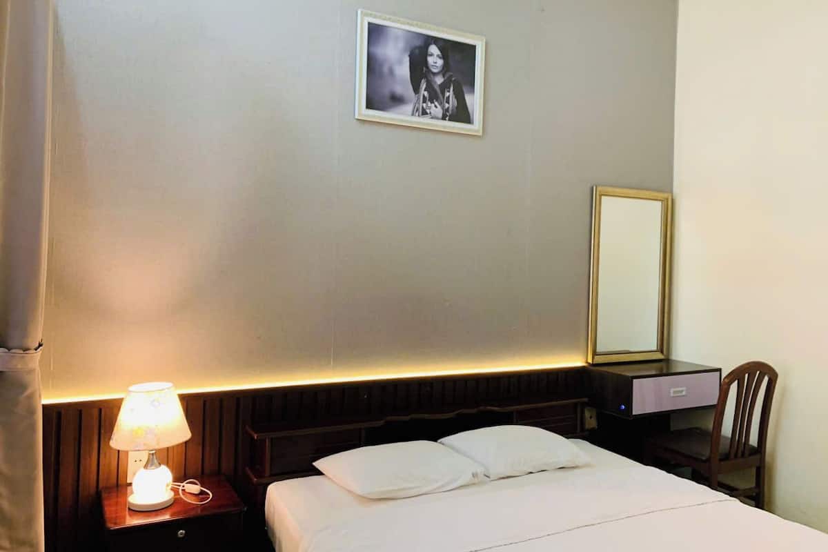Habitación de hotel con cama, mesita de noche con lámpara, escritorio con silla y un cuadro en la pared.