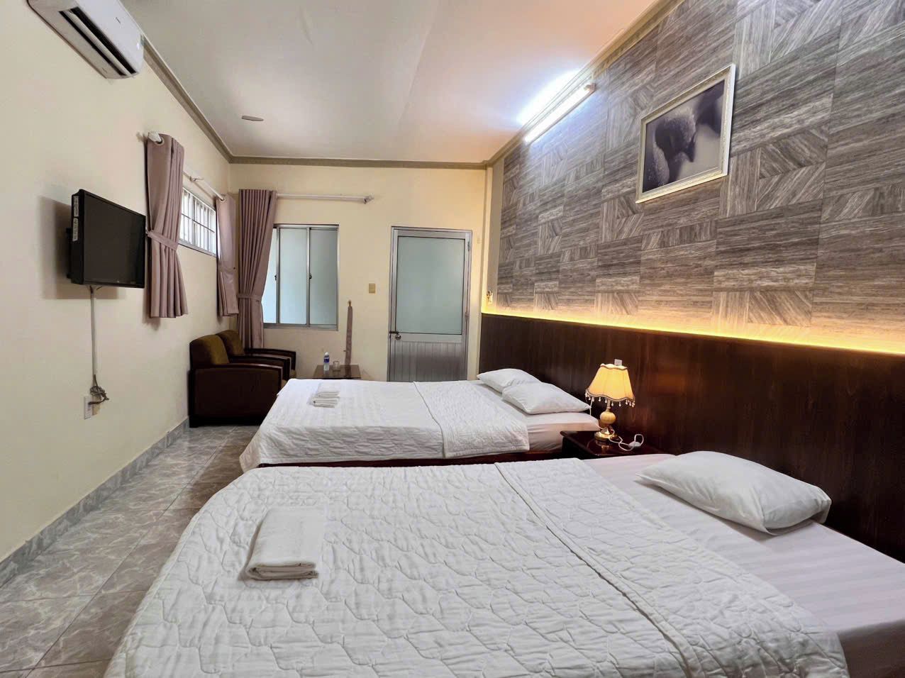 A hotel room with two beds, a television, a wall-mounted picture, and a wooden headboard.