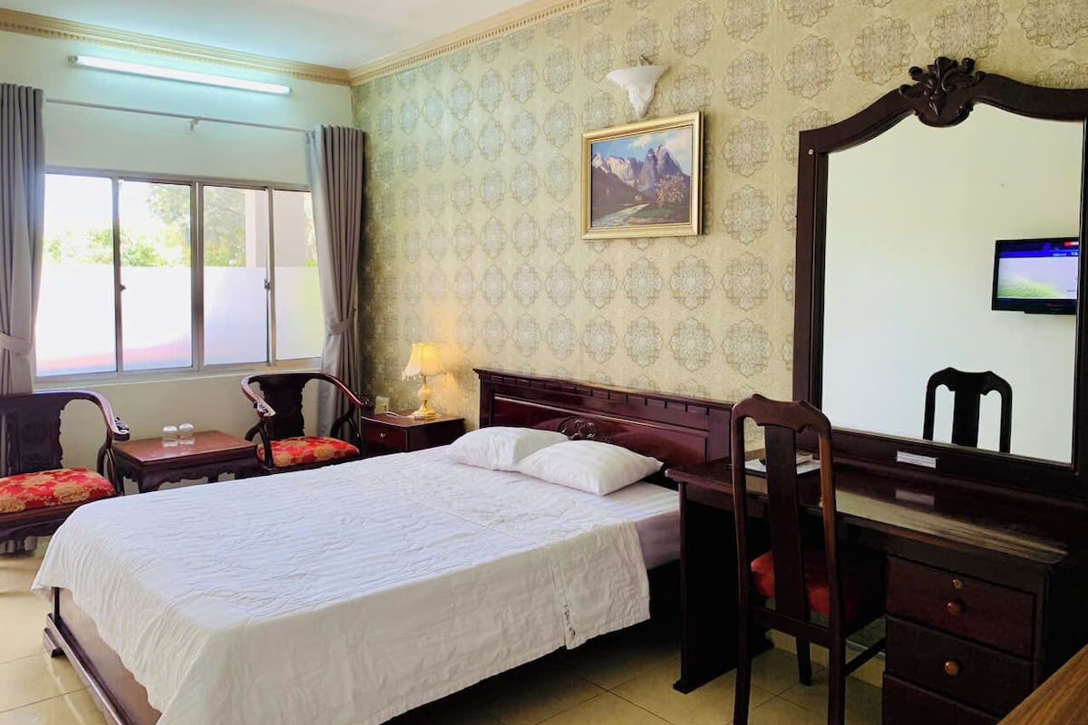 Habitación de hotel con una cama grande, un escritorio, una silla, un espejo y una ventana con cortinas.
