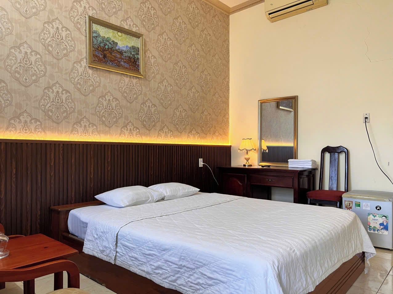 Une chambre d’hôtel équipée d’un lit, d’un bureau, d’une chaise, d’un miroir et d’un climatiseur fixé au mur.