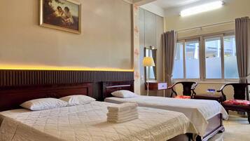 A hotel room with two beds, a painting on the wall, a lamp, and a view of the outside through the window.
