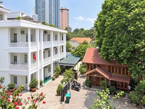 Un edificio de varios pisos con balcones, un patio con plantas en macetas y una casa tradicional con techo rojo.