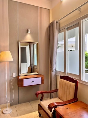 Una habitación con un escritorio de madera, una silla, un espejo, una lámpara y una ventana con cortinas.