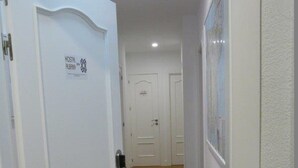 Un pasillo con puertas blancas, un cartel en una de las puertas y suelo de baldosas.