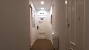 Un pasillo estrecho con piso de madera y paredes blancas, que conduce a una puerta con un letrero encima.