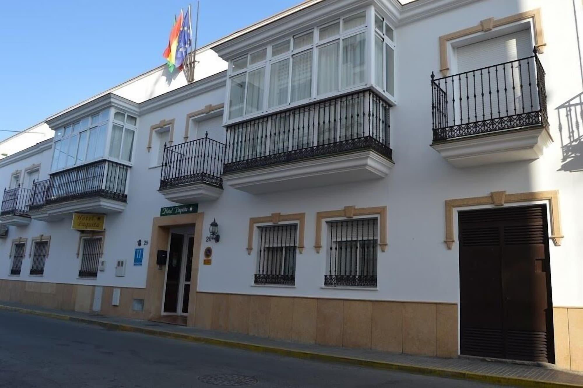 Un edificio blanco con balcones, una puerta con la leyenda 'Hotel Puerta' y una bandera en la parte superior.