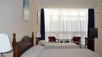 Habitación de hotel con dos camas, un escritorio, sillas, un televisor y una ventana con cortinas.
