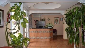 Una habitación amplia con suelo de baldosas, un mostrador de recepción y varias plantas en macetas.
