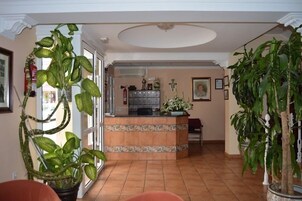 A spacious room with a tiled floor, a reception desk, and several potted plants.