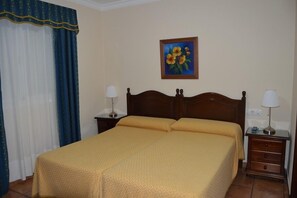 A hotel room with a large bed, two bedside tables, a painting on the wall, and a window with curtains. - Hotel Paquita (Chipiona)