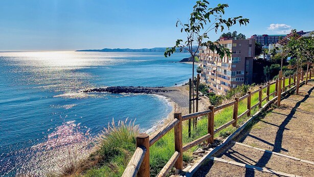 A coastal view with a wooden walkway, beach, and buildings in the background.