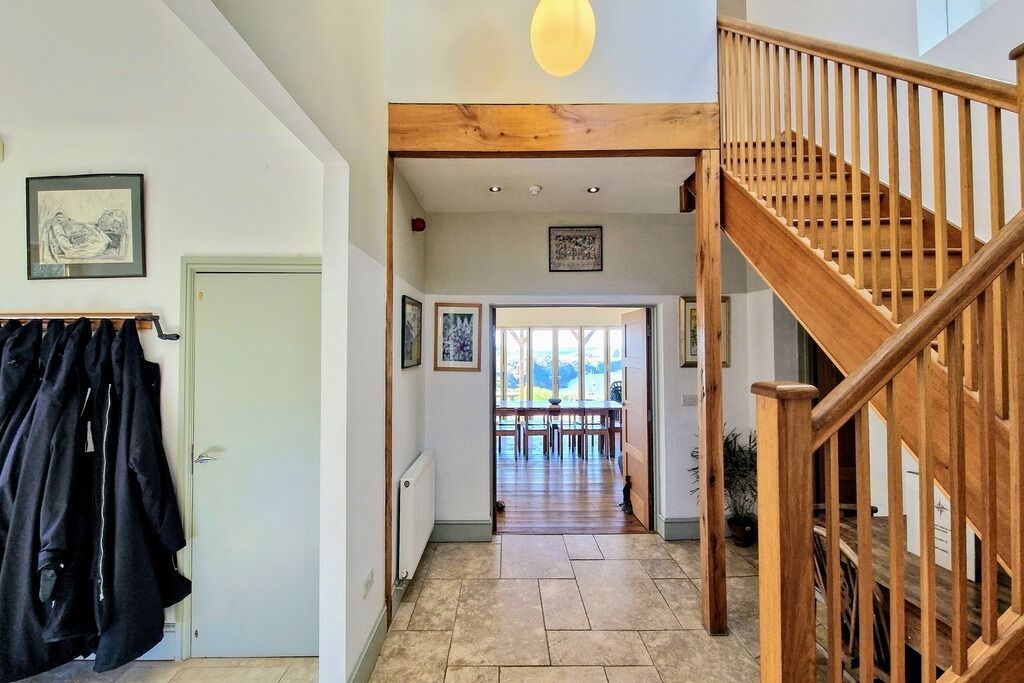 A hallway with a wooden staircase, a coat rack, and a dining area with a view.