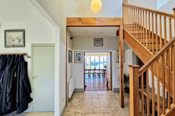 A hallway with a wooden staircase, a coat rack, and a dining area with a view.