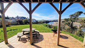 A covered patio with a picnic table and a wheelbarrow, overlooking a coastal landscape with houses and a river.