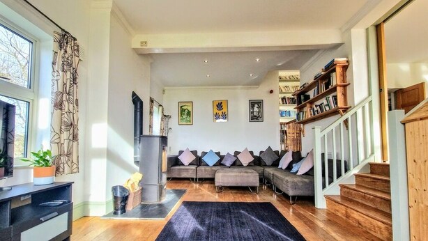 Ein Wohnzimmer mit Ecksofa, Kamin, Treppe und Bücherregal.