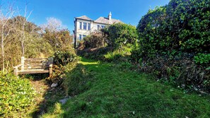 Un jardin avec un banc, un feuillage dense et une maison en arrière-plan.