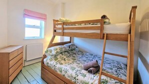 Ein Schlafraum mit Etagenbett, Fenster, Heizkörper und einem hölzernen Nachttisch.