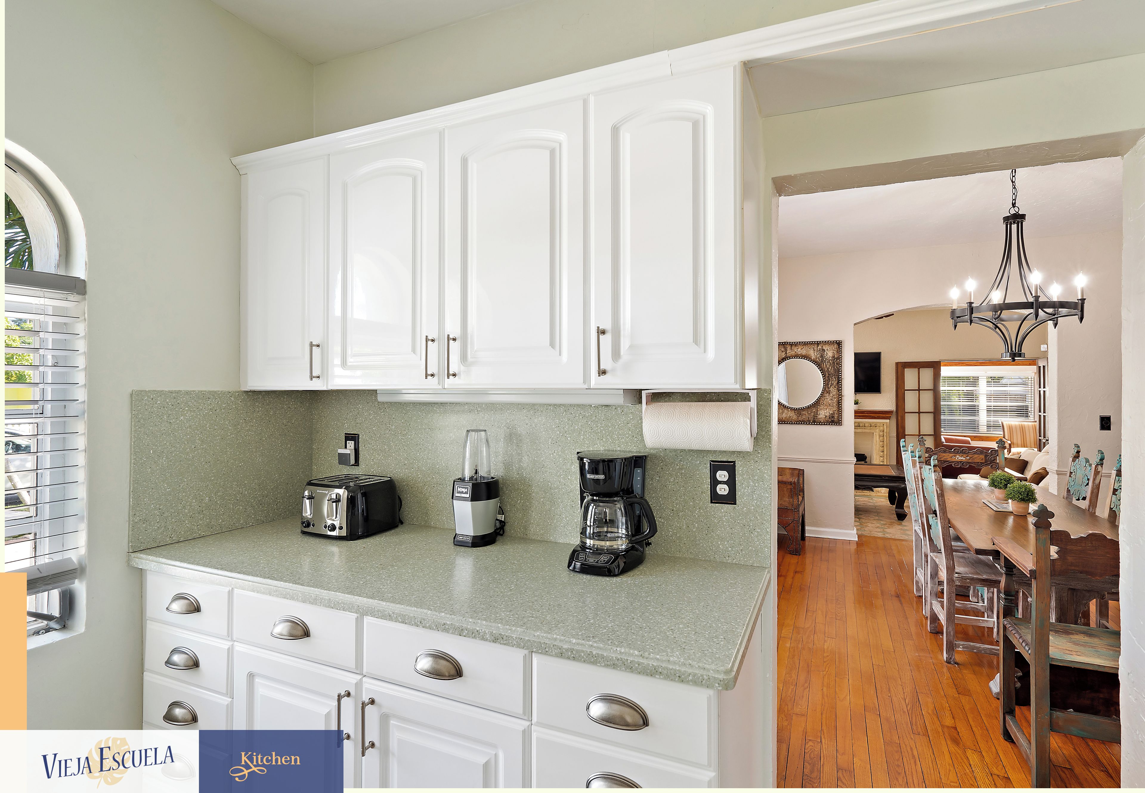 A kitchen with white cabinets, a granite countertop, a toaster, a coffee maker, and a dining area with a wooden table and chairs.
