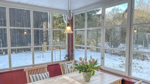 A conservatory with a wooden table and chairs, a vase of flowers, and a view of a snow-covered yard. - traumHaff Protected monument Malchen's yard, sauna, open fireplace, fenced meadow (Ahlbeck OT Gegensee)