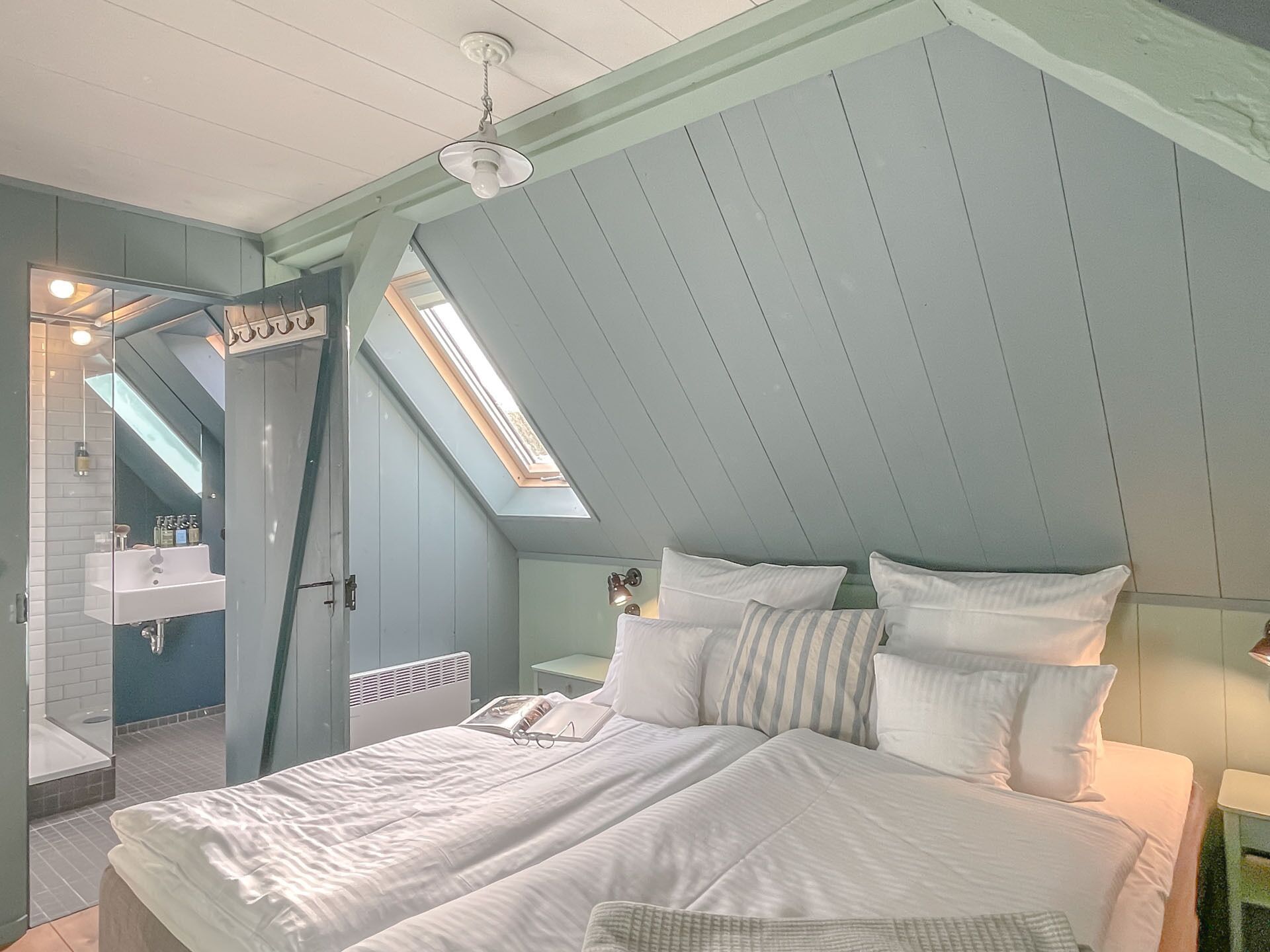 A bedroom with a sloped ceiling, a skylight, a bed with white bedding, and a small bedside table.
