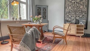 A cozy room with a wooden floor, two wicker chairs, a wooden table, and a large tapestry on the wall. - traumHaff Protected monument Malchen's yard, sauna, open fireplace, fenced meadow (Ahlbeck OT Gegensee)