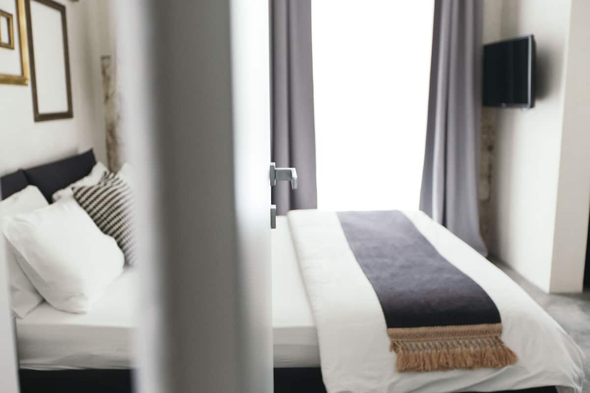 Une chambre d’hôtel avec un lit, un téléviseur fixé au mur et une fenêtre avec des rideaux.