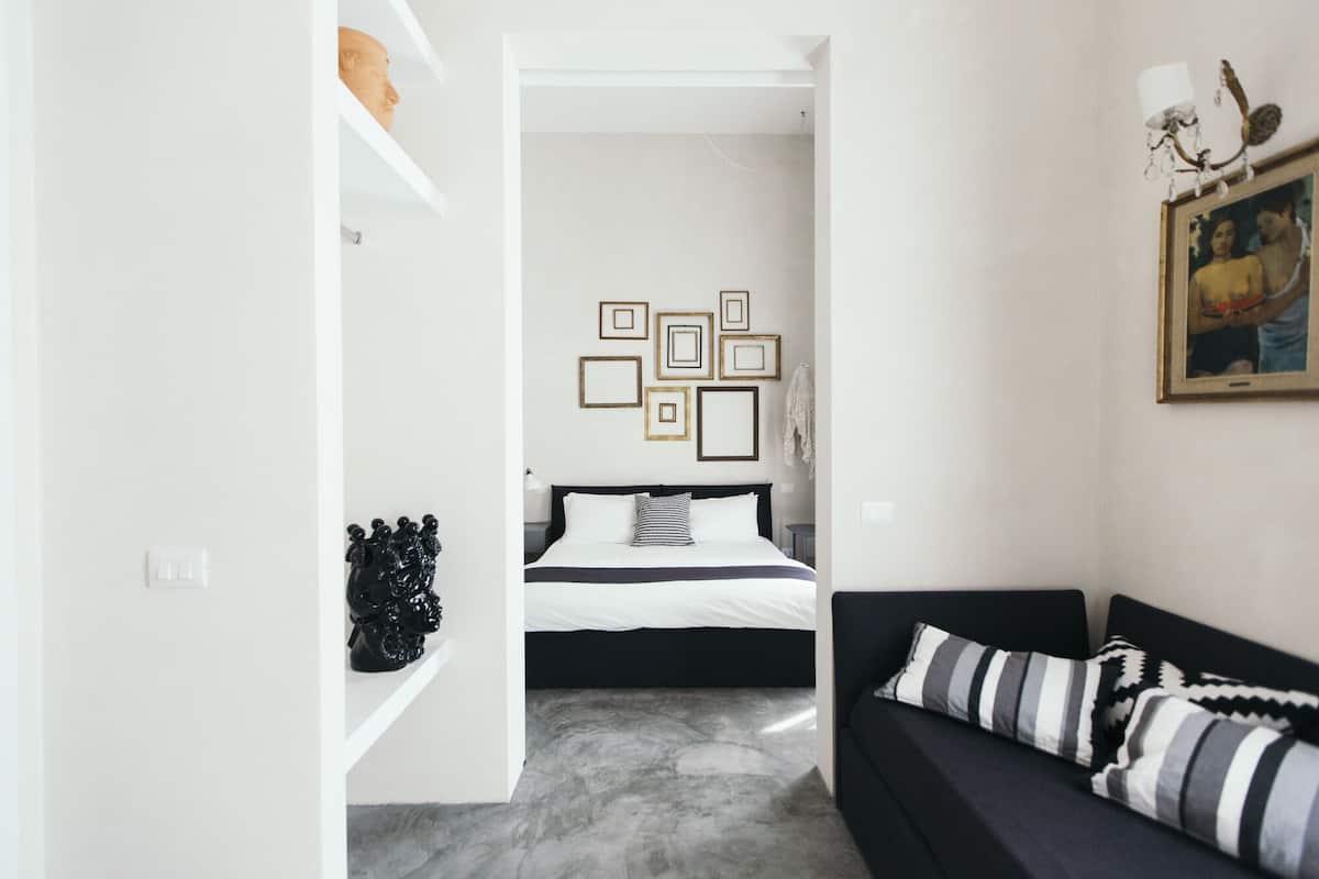Une chambre moderne avec un lit, un canapé noir et un couloir menant à une autre pièce.