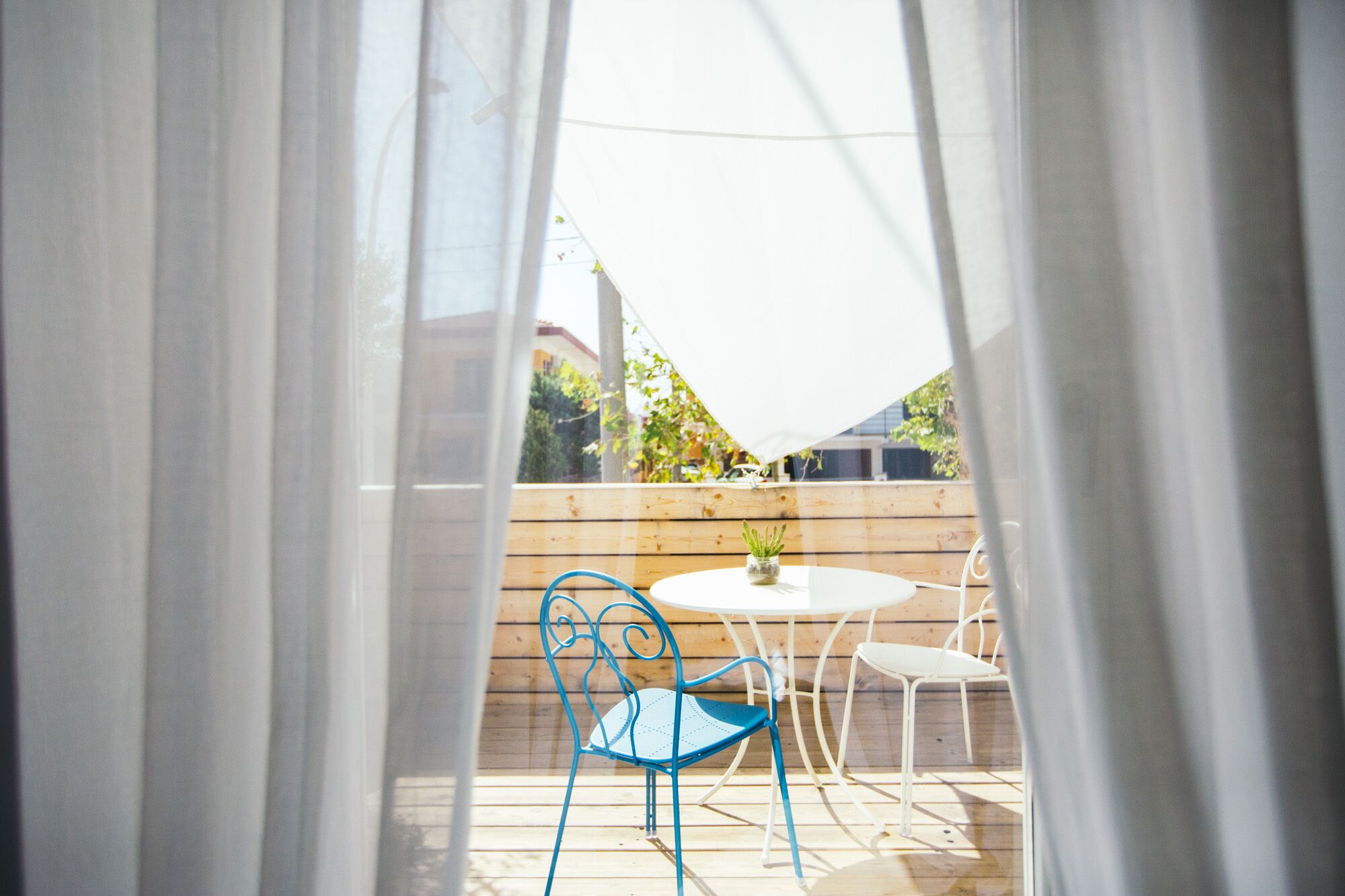 Een terras met een ronde tafel en twee stoelen, een kleine potplant en een houten omheining.