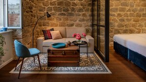 Una habitación acogedora con pared de piedra, un sofá, una silla azul, un cofre de madera y una cama.
